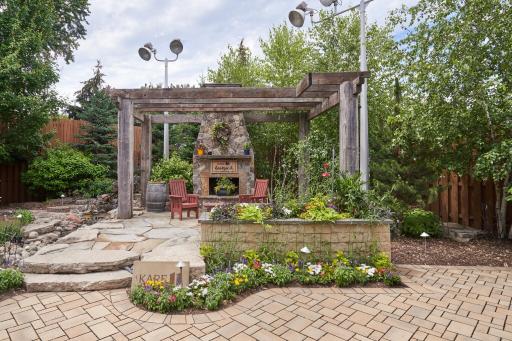 permeable paver patio with colorful flowers and a custom fireplace and pergola
